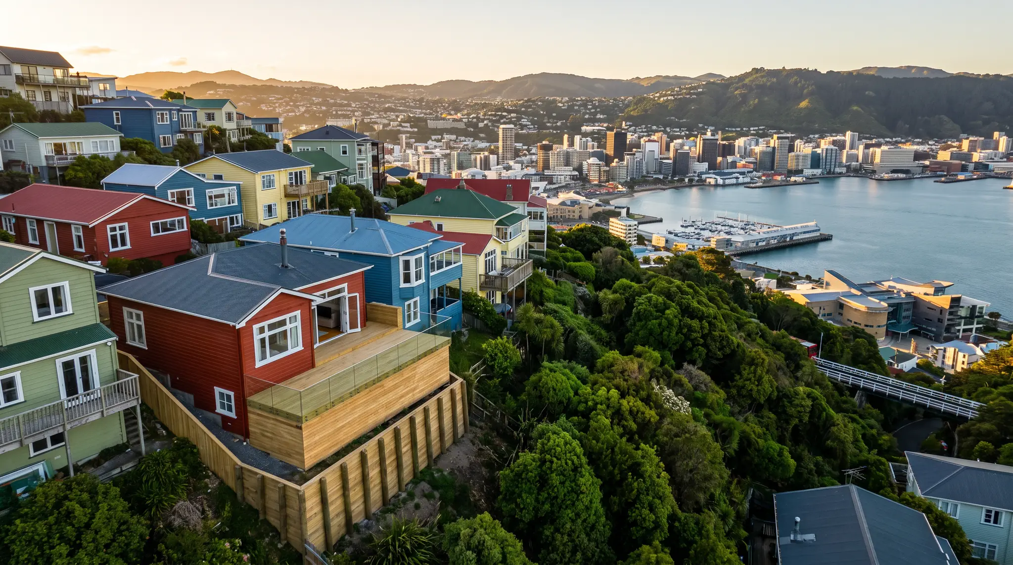 Timber houses on a steep Wellington hillside with a new retaining wall and deck, above the harbour and city